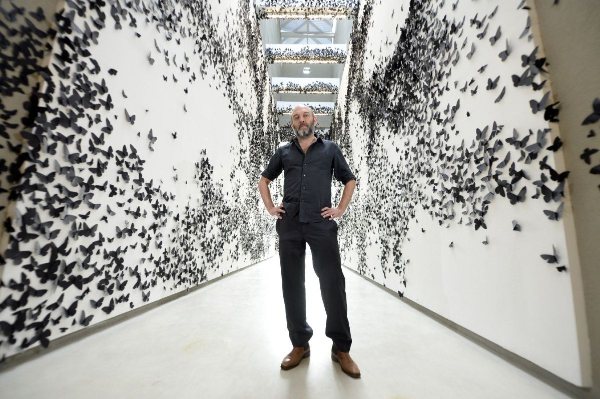Carlos Amorales staat tussen kunstwerk van witte wanden met zwarte vlinders